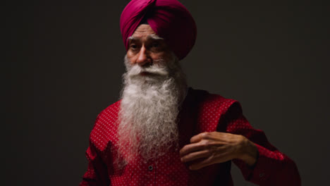 Low-Key-Studio-Lighting-Shot-Of-Senior-Sikh-Man-With-Beard-Tying-Fabric-For-Turban-And-Using-Salai-Needle-Against-Dark-Background-2